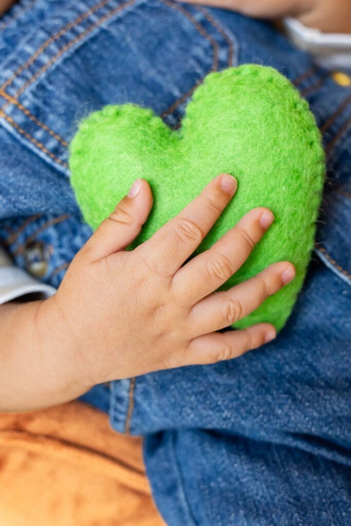 Newborn baby tiny handing holding green heart toy during photoshoot in pittsburg ks
